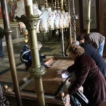 Pilgrims kneeling beside the Stone of Anointing under hanging lamps in the Church of the Holy Sepulchre.