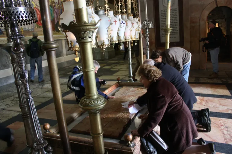 Pilgrims kneeling beside the Stone of Anointing under hanging lamps in the Church of the Holy Sepulchre.