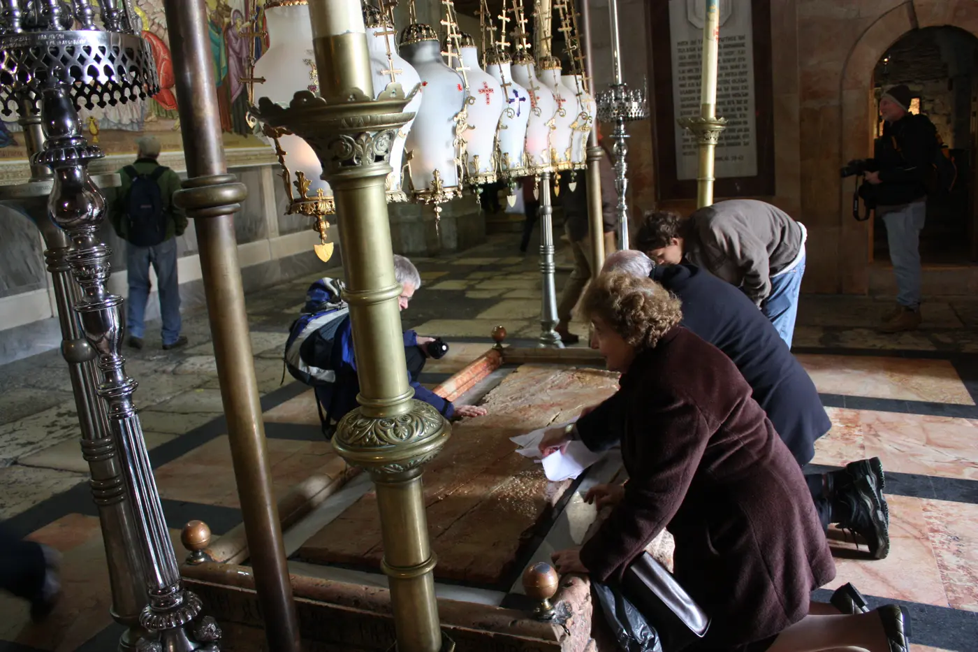 Pilgrims kneeling beside the Stone of Anointing under hanging lamps in the Church of the Holy Sepulchre.